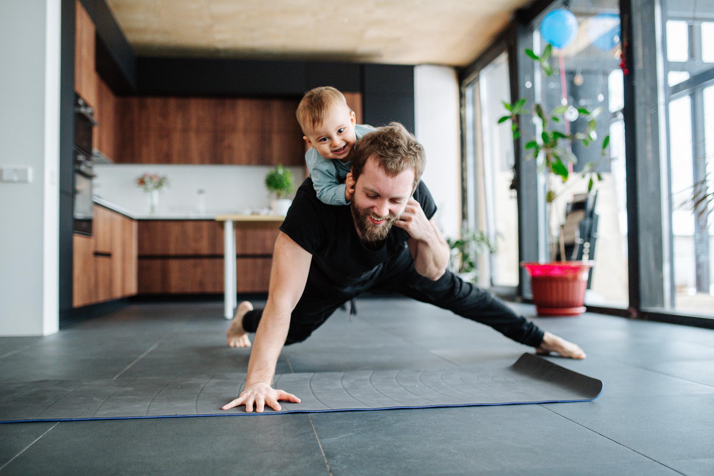Father working out in living room with small child climbing atop his back